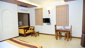 A hotel room with a bed, a sofa, a dining table with chairs, a TV, and a window with blinds. - Hotel Leaf on Lagoon (Seeduwa - Katunayake)
