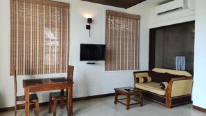 A living room with a wooden table, two chairs, a sofa, and a TV. - Hotel Leaf on Lagoon (Seeduwa - Katunayake)