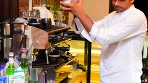 A barista preparing a drink behind a counter with coffee machines and various beverage containers. - Hotel Leaf on Lagoon (Seeduwa - Katunayake)