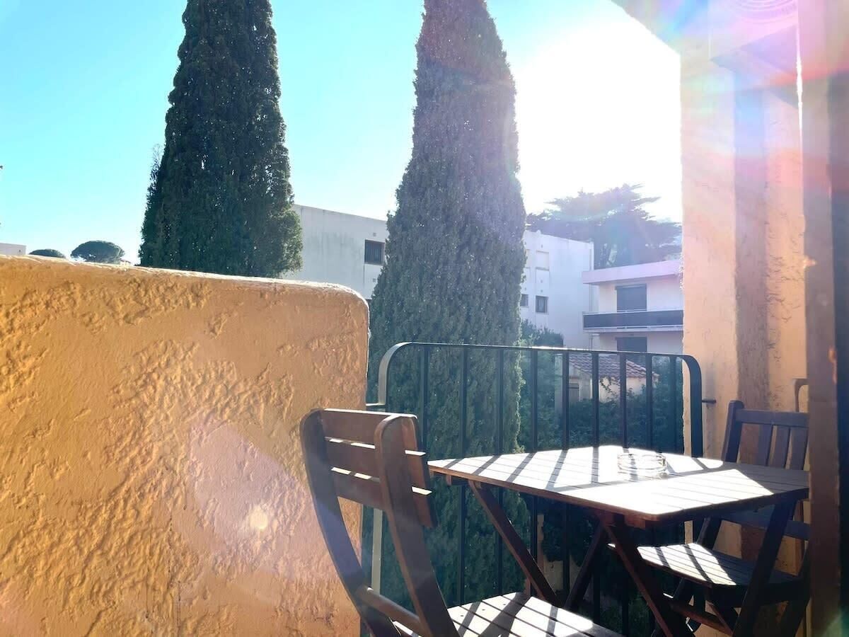 Une terrasse extérieure avec une table et des chaises, entourée d’un petit muret et de grands arbres.