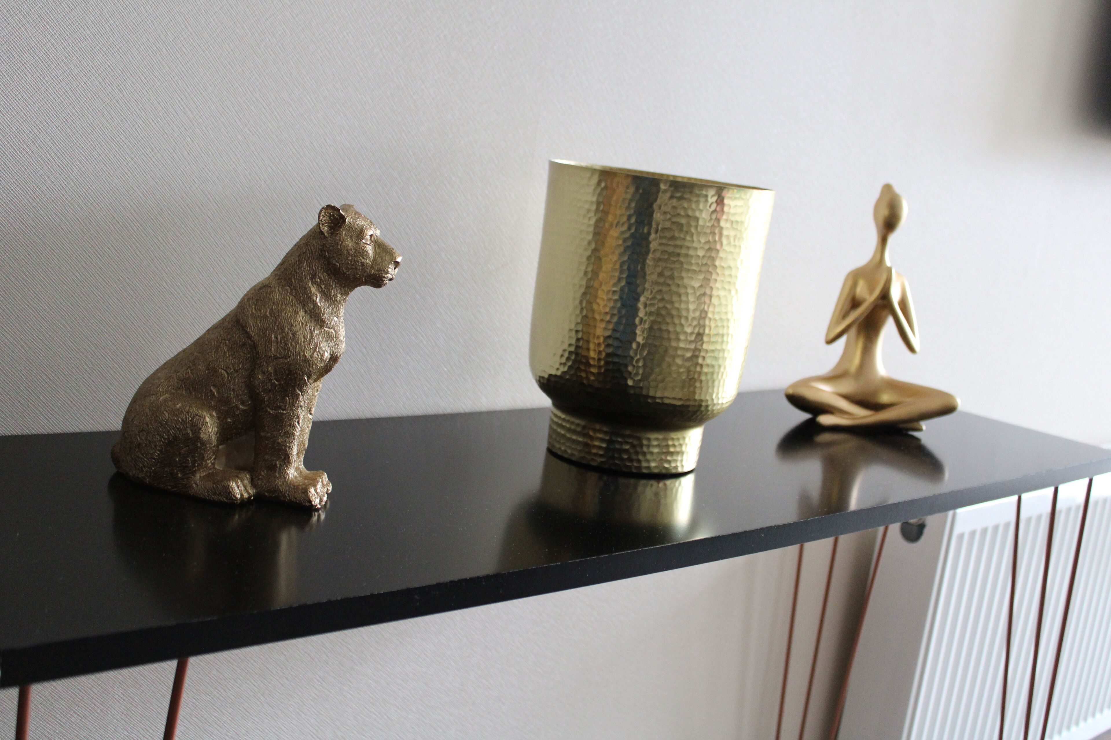 A black shelf with a bear figurine, a textured golden cup, and a meditating figure.