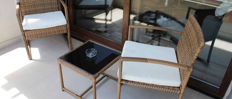 Un balcón con sillas de mimbre y una mesa de vidrio.