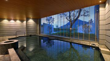 Una piscina interior moderna con vistas despejadas al exterior gracias a un amplio ventanal, techo de madera y pared de piedra.
