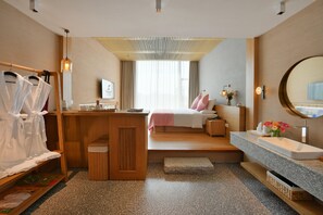 Una habitación de hotel moderna con un escritorio de madera, una cama con ropa de cama rosa, un espejo grande y un baño con encimera de granito.
