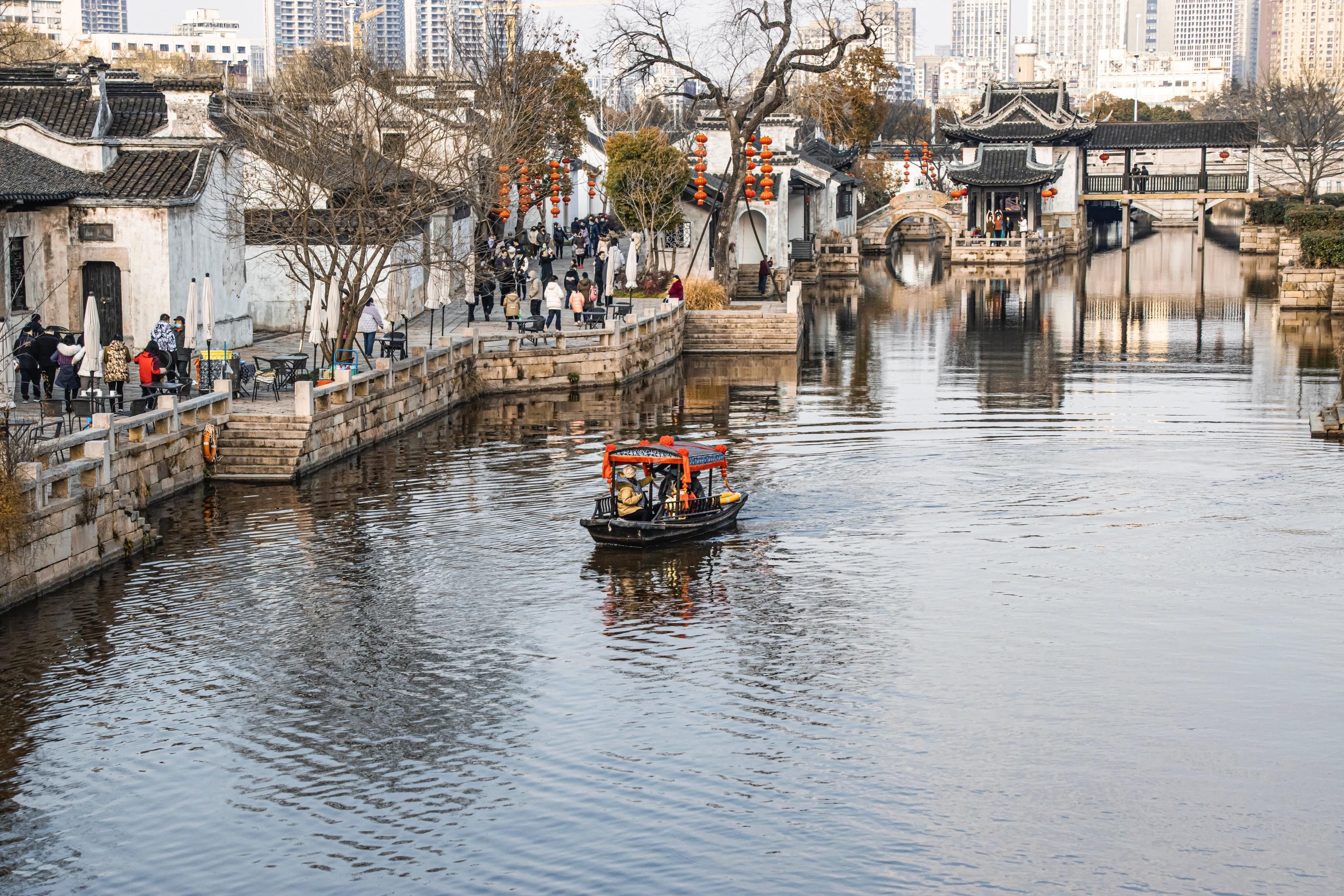 A traditional Chinese water town with a boat on the river, stone bridges, and traditional buildings.