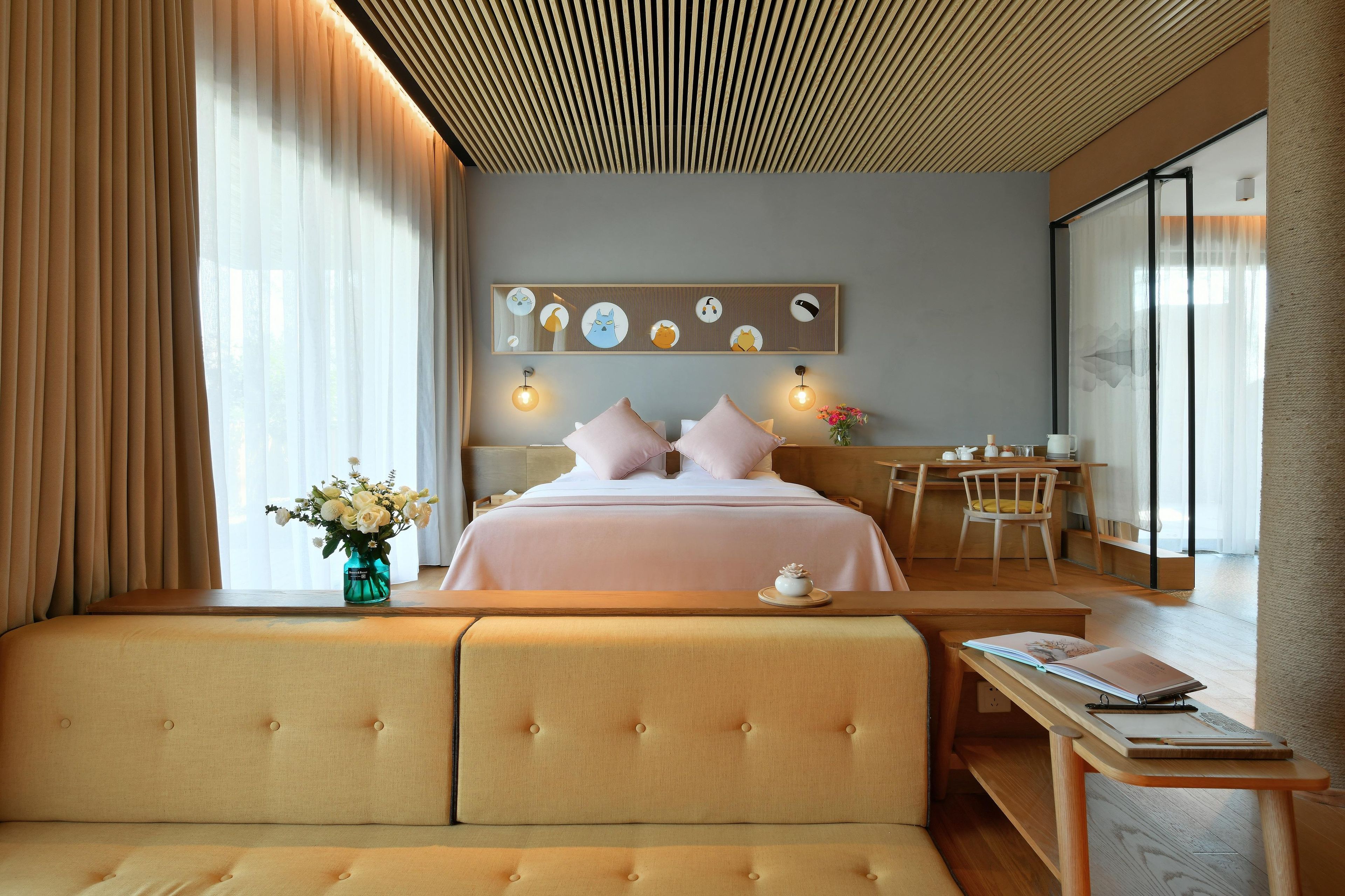 Quarto de hotel moderno com uma cama grande, área de estar, escrivaninha e obra de arte na parede.
