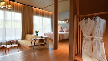 A modern hotel room with a sofa, a bed, a desk, and a robe rack.