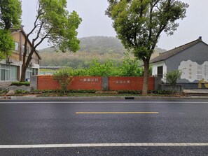 A gated entrance with a wooden fence and a sign, a road with a yellow line, and buildings with traditional architecture. - Blossom Hill Hotel Wuxi Yangshan (Wuxi)