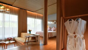 A modern hotel room with a wooden floor, a sofa, a bed, a sitting area with a table, and a rack with robes. - Blossom Hill Hotel Wuxi Yangshan (Wuxi)
