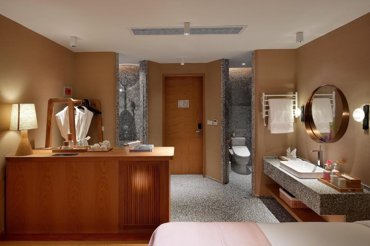 A hotel bathroom with a wooden vanity, a sink, a mirror, and a toilet.