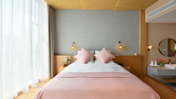 Una habitación de hotel con una cama grande, cabecera de madera, mesitas de noche, un espejo y un baño con lavamanos y espejo.