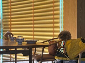 A dining area with a table set for two, featuring a bowl, a cup, and a glass. A dog is seated at the table, and a yellow jacket is draped over a chair. - Blossom Hill Hotel Wuxi Yangshan (Wuxi)