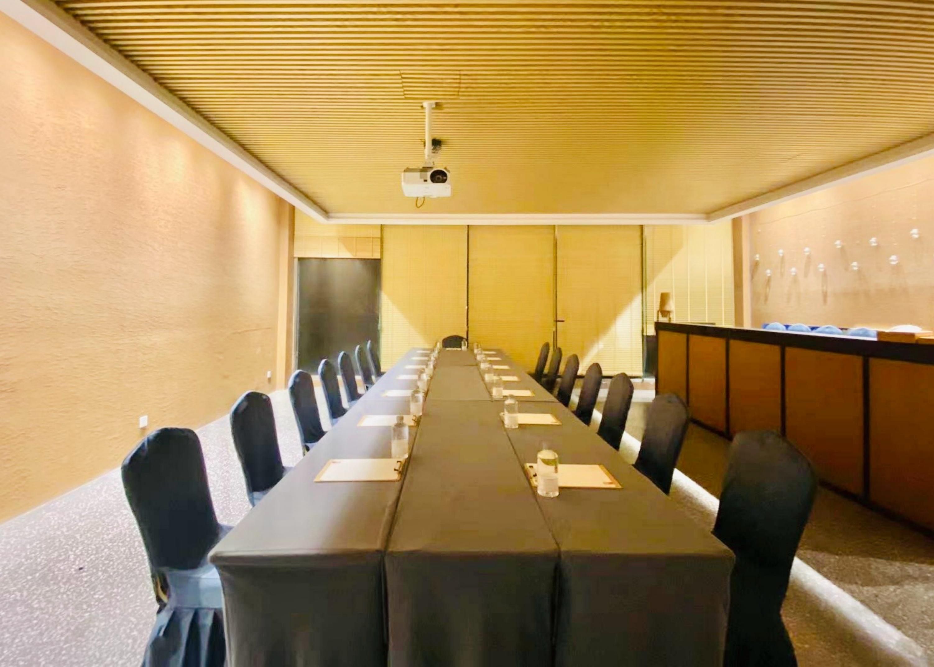Una sala de conferencias con una larga mesa, sillas, un proyector y un dispensador de agua.