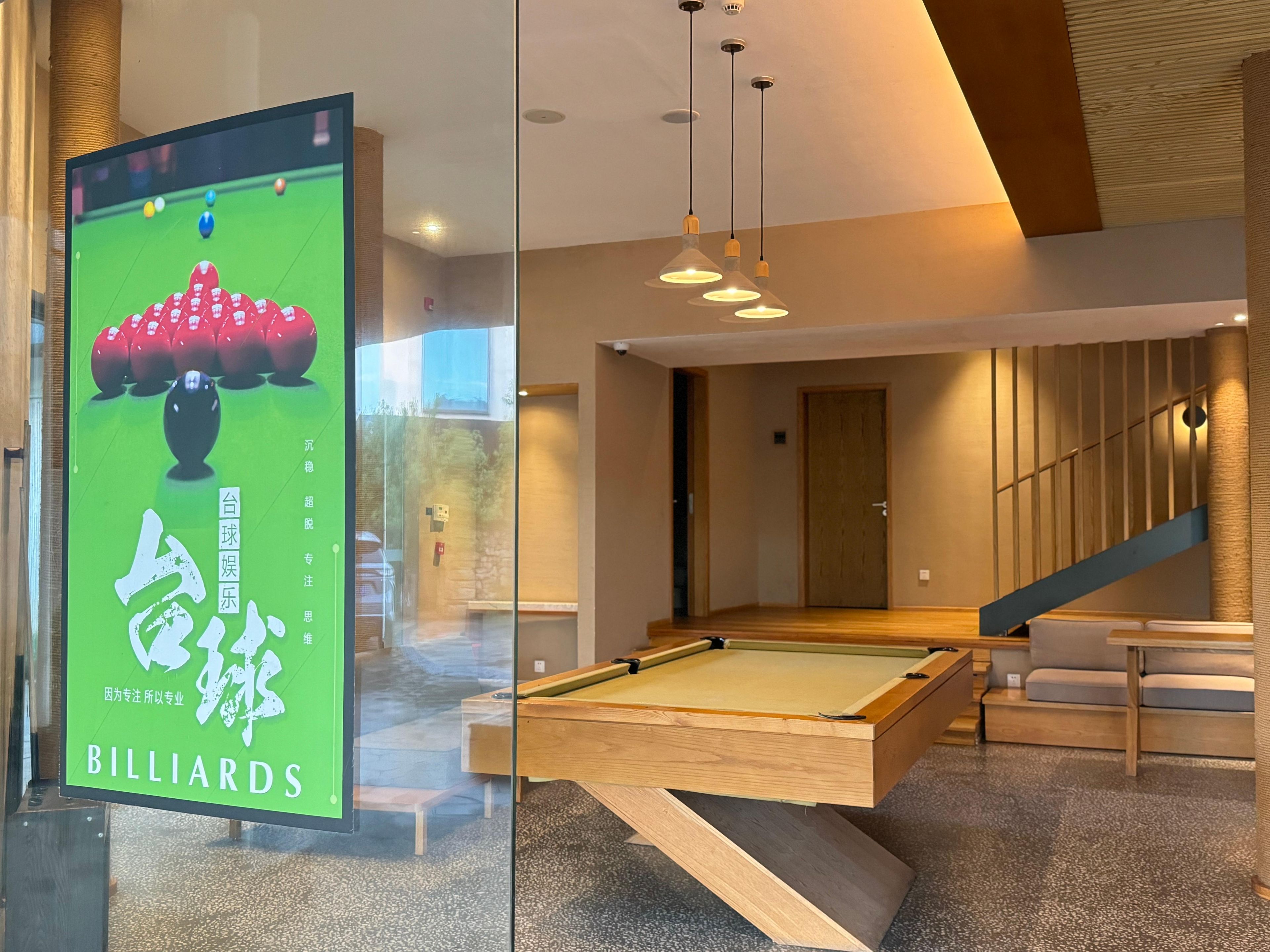 A billiards room with a pool table, a glass partition with a poster, and a staircase.