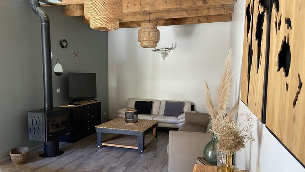 En hyggelig stue med brændeovn, sofa, sofabord og fjernsyn.