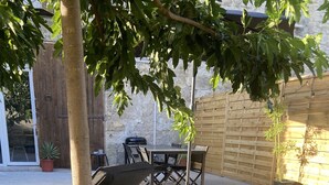 En patio med et bord, stole, grill og en potteplante.