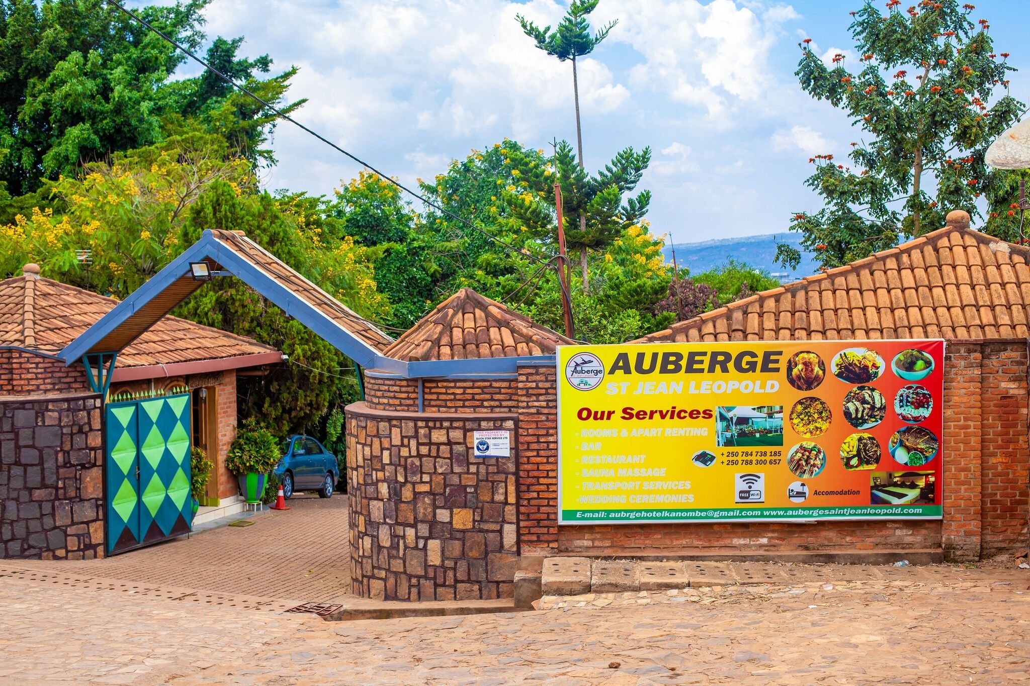 Entrada de un hotel con fachada de piedra, una puerta azul y verde, y un cartel anunciando servicios como habitaciones, restaurante y masajes.