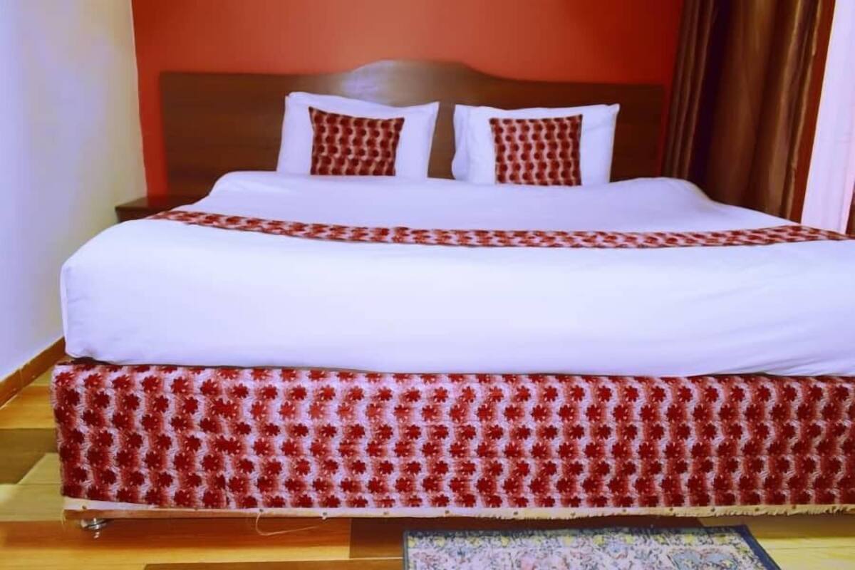 A double bed with a white and red patterned bedspread, a wooden headboard, and a red and white patterned skirt.