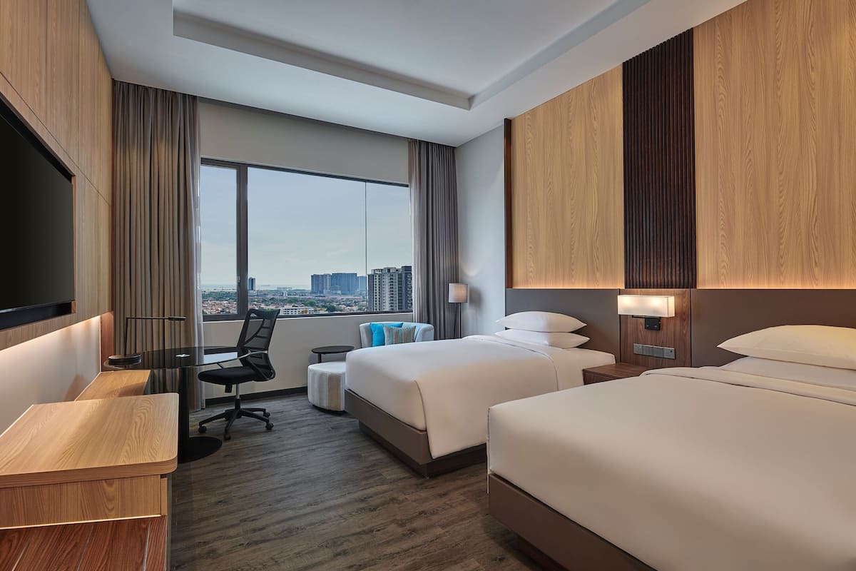 Une chambre d’hôtel avec une grande fenêtre, un bureau, deux lits et un téléviseur.