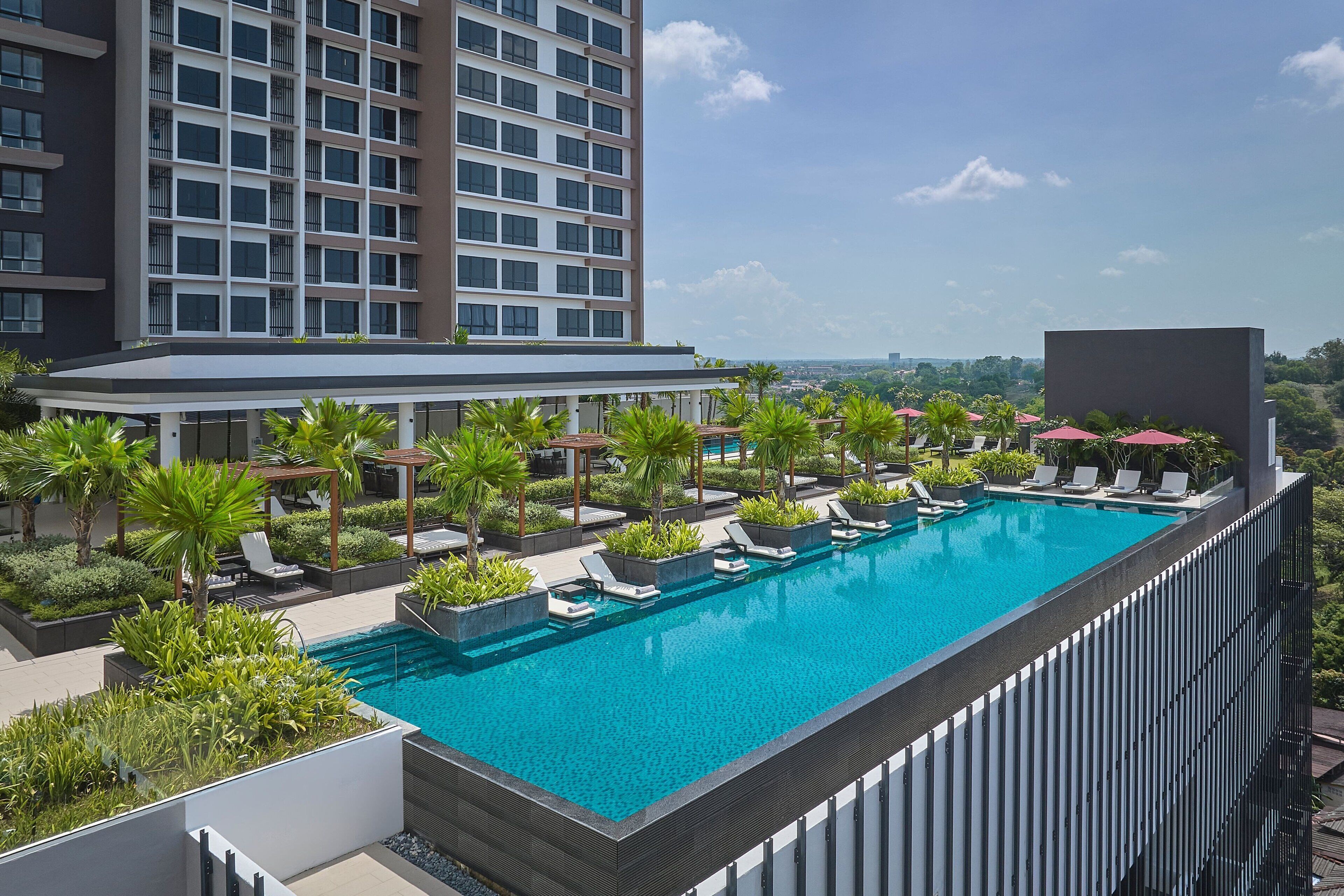 A rooftop swimming pool with lounge chairs and palm trees, surrounded by a modern building.