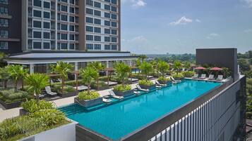 A rooftop swimming pool with lounge chairs and palm trees, surrounded by a modern building.