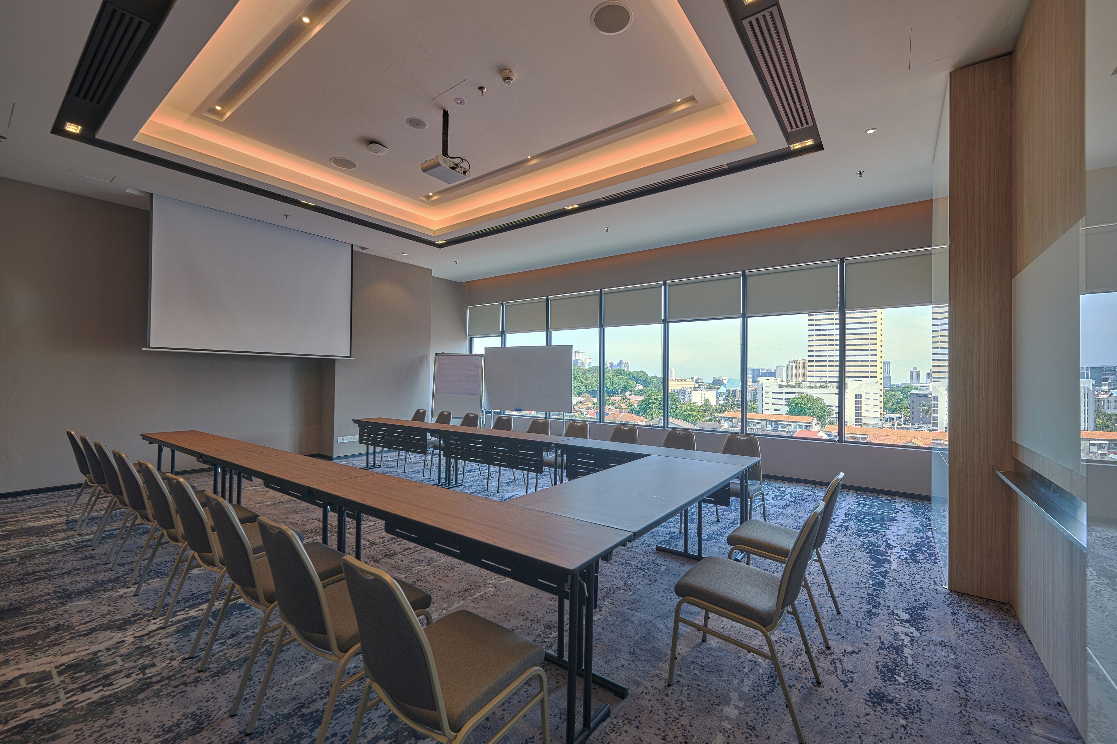 Un salón de conferencias con una larga mesa, sillas, una pantalla de proyector y grandes ventanas que ofrecen vistas a la ciudad.