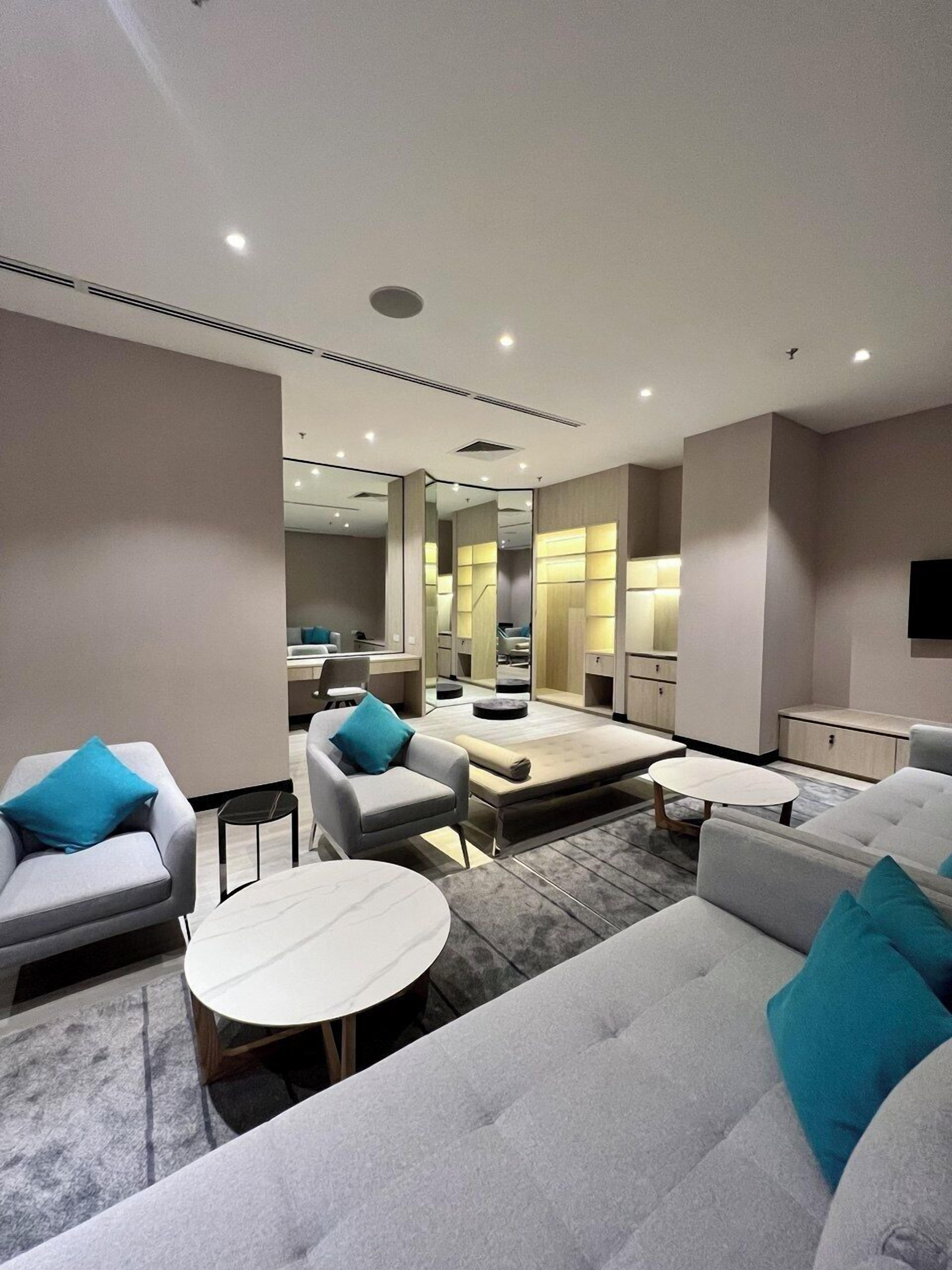 A modern hotel room with a sofa, armchairs, a small table, and a mirror.