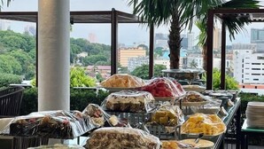 Un buffet est installé sur des tables, avec une variété de plats et de boissons, le tout mis en valeur par un décor représentant un paysage urbain et de la verdure.