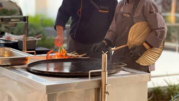 Un chef preparando comida en una parrilla grande al aire libre, con un hombre ayudando.