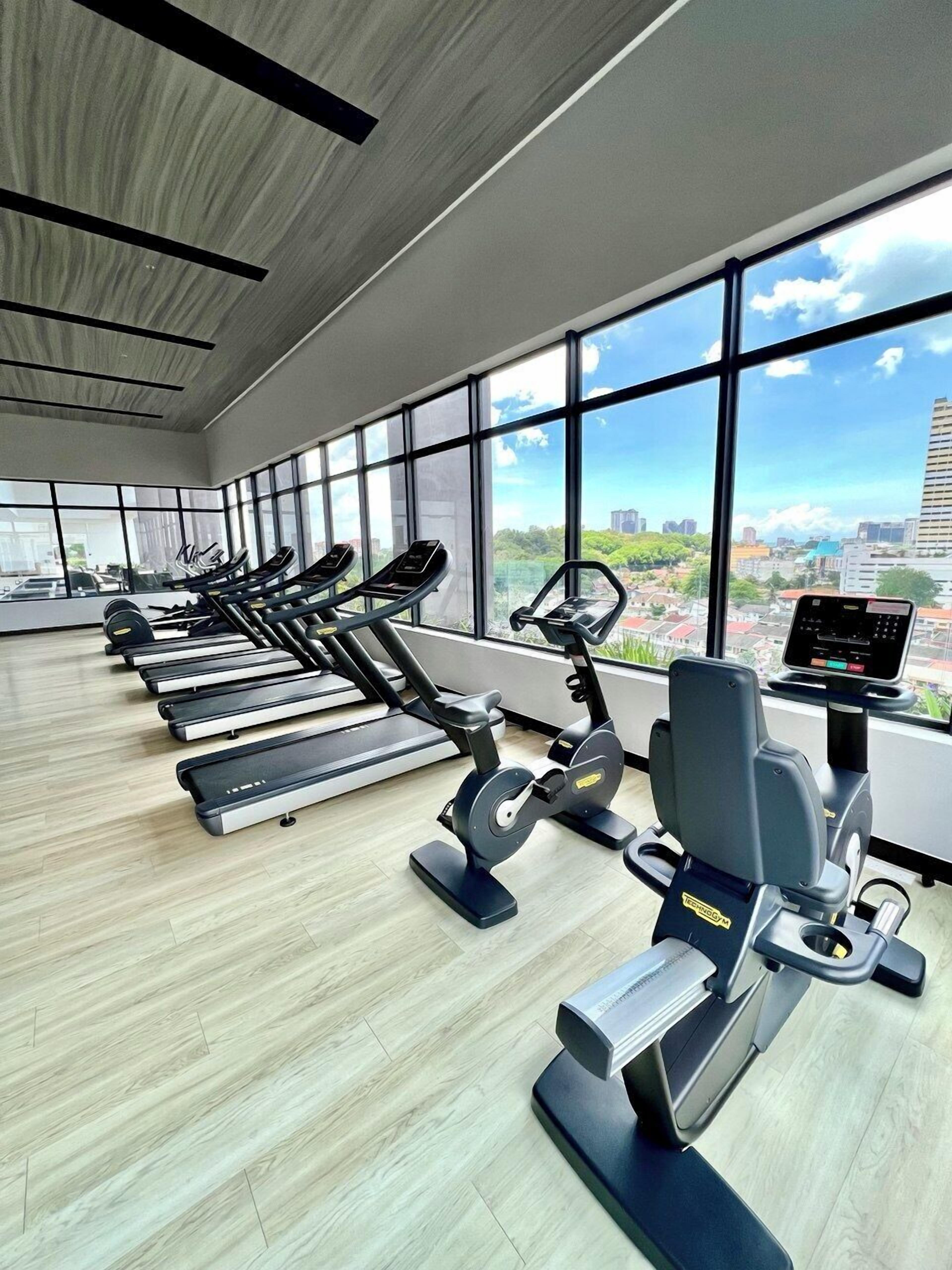 Een fitnessruimte met loopbanden en elliptische trainers, grote ramen en uitzicht over de stad.