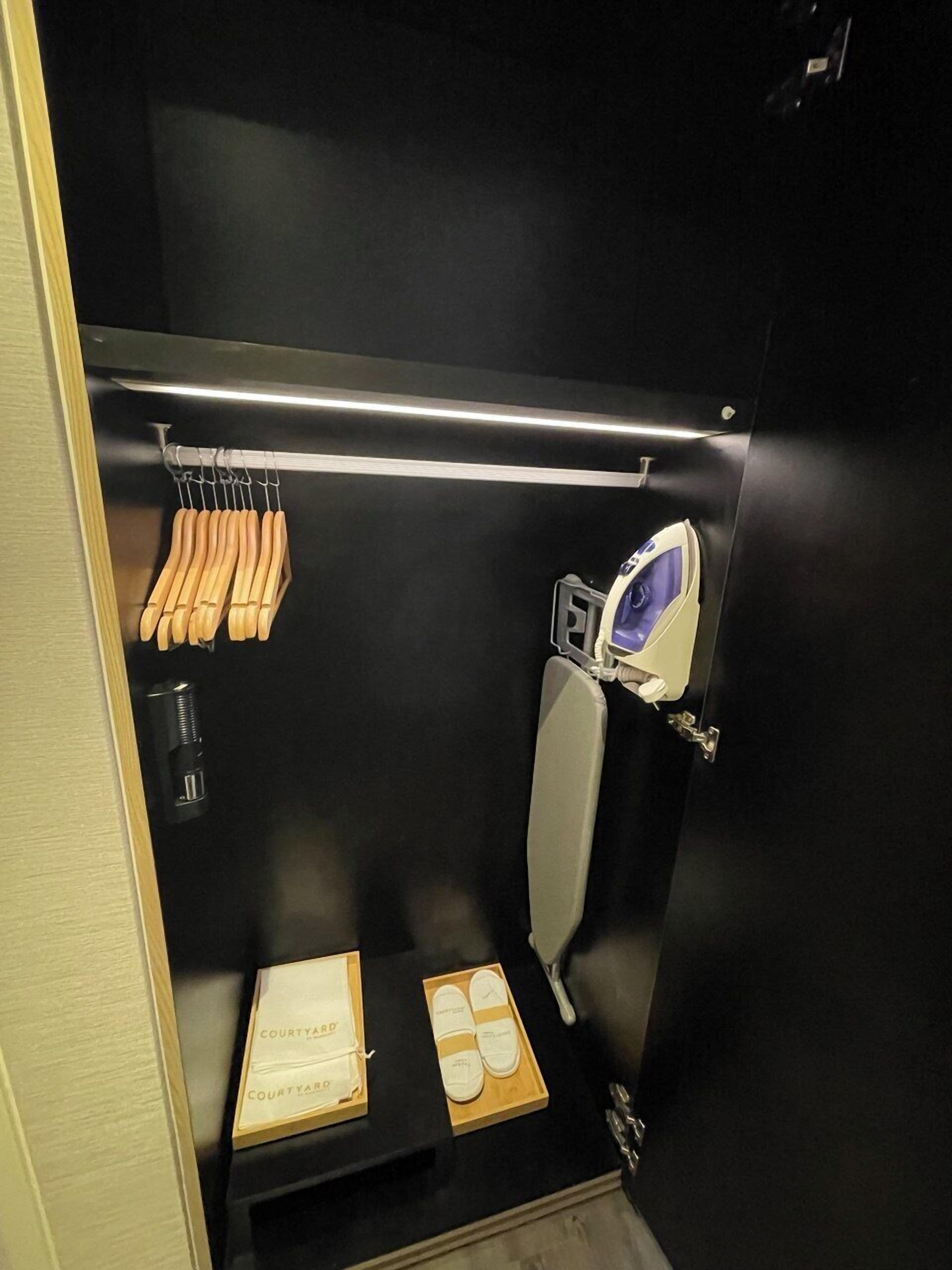 Un baño pequeño y funcional con inodoro, secamanos, toallero y un estante con artículos de aseo.