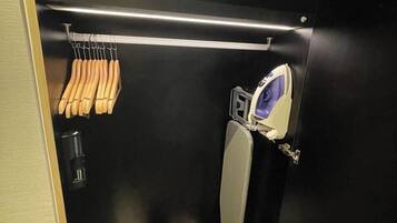Un baño pequeño y funcional con inodoro, secamanos, toallero y un estante con artículos de aseo.
