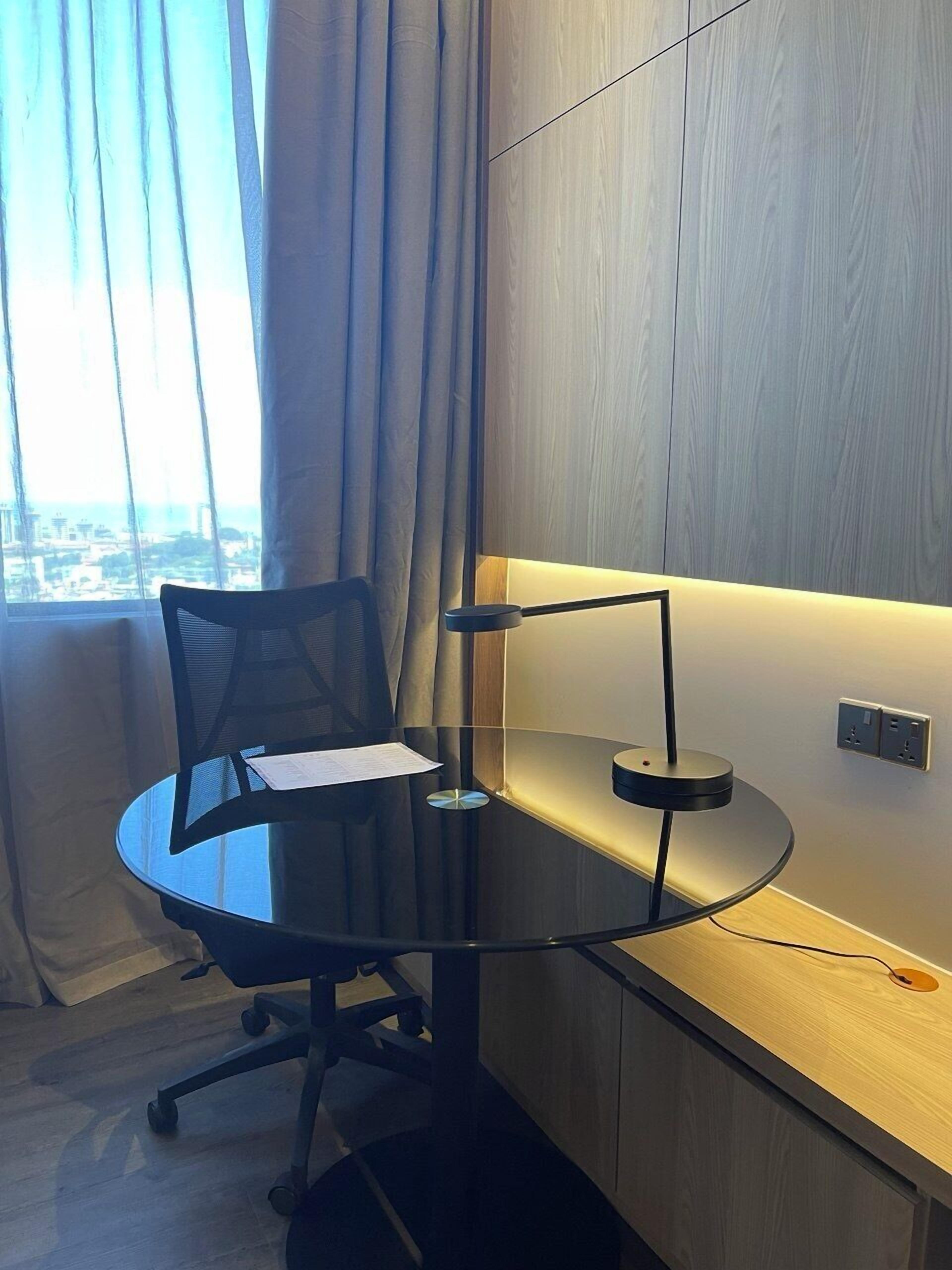 A modern office space with a glass table, black office chair, and a desk lamp.