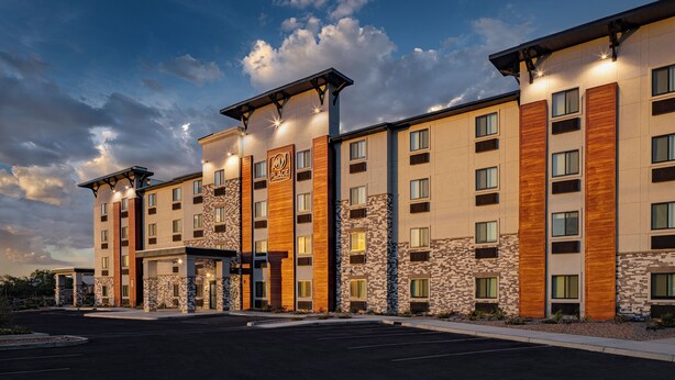 Un hotel de varios pisos con un diseño moderno, que combina paneles de piedra y madera, ventanas amplias y una entrada bien iluminada.