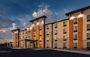 A multi-story hotel with a modern design, featuring a mix of stone and wood paneling, large windows, and a well-lit entrance. - My Place Hotel-Tucson South AZ (Tucson)