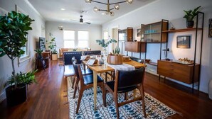 A modern kitchen with wooden cabinets, a dining table, and chairs. There are potted plants and a chandelier.