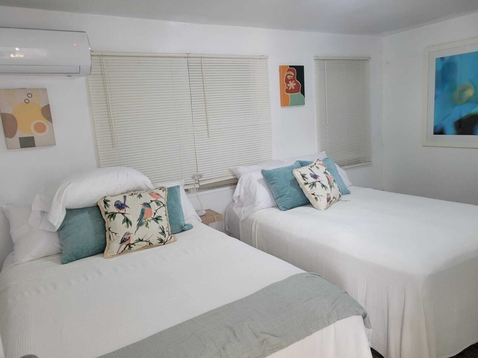 A hotel room with two single beds, white bedding, and a window with blinds.