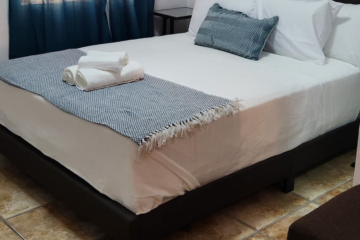 Una cama bien hecha con una colcha azul y blanca a rayas, un cabecero oscuro y una almohada.