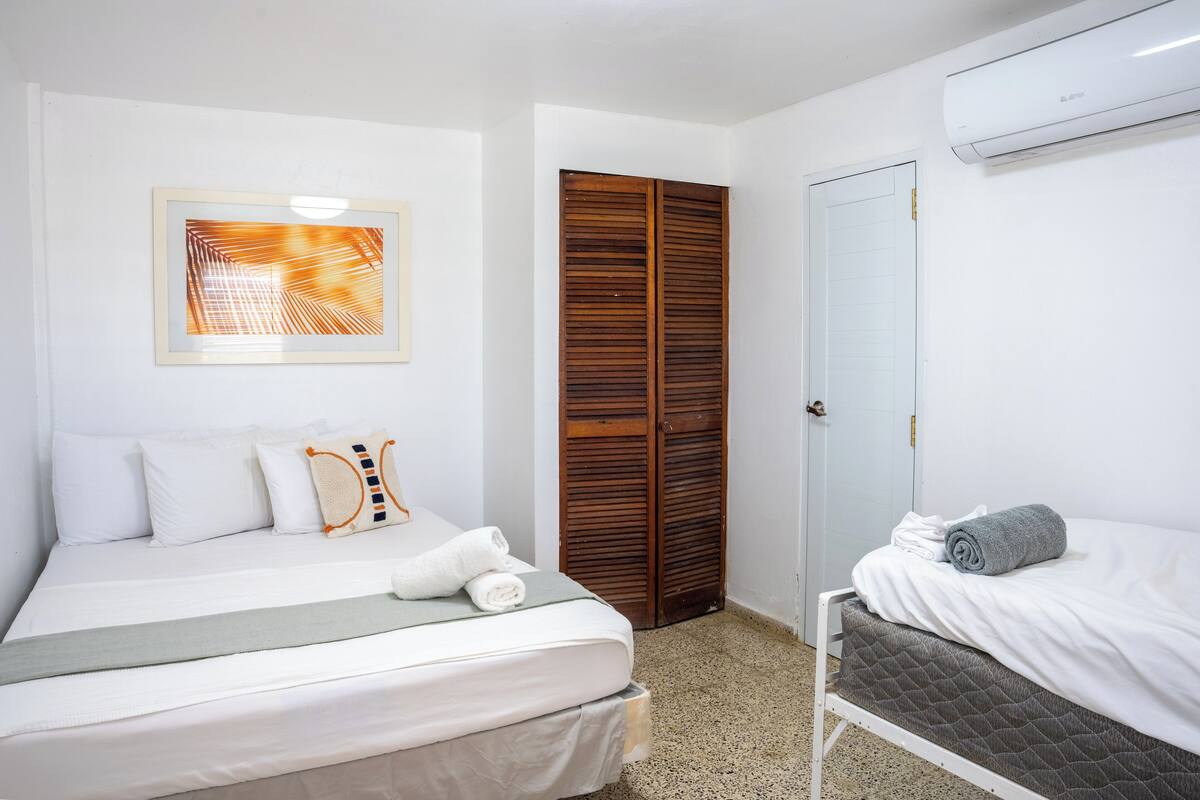 Una habitación de hotel con cama, mesita de noche, armario y aire acondicionado.