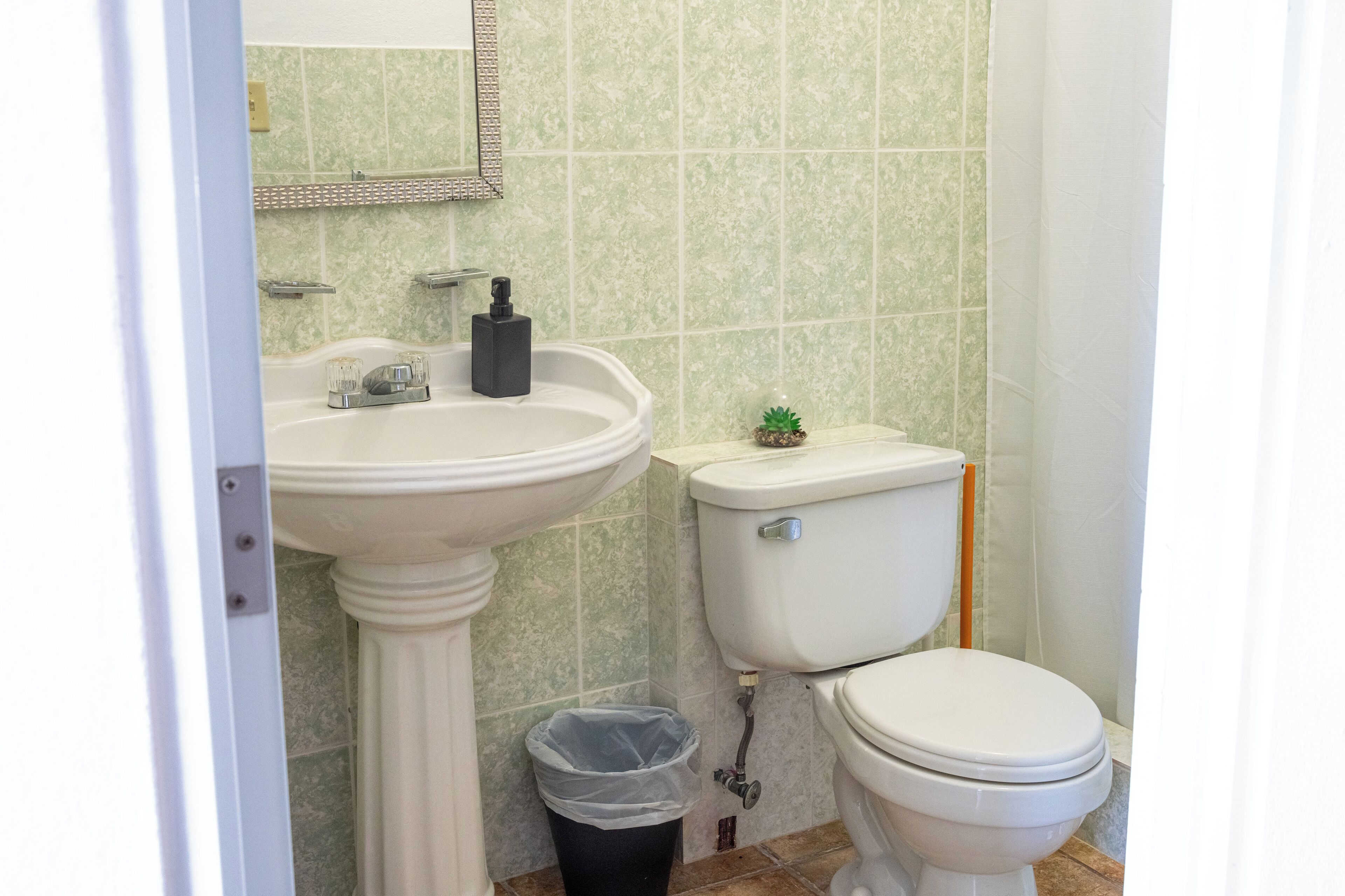 A bathroom with a pedestal sink, toilet, and a trash bin.