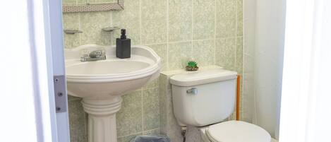 Un baño con lavamanos pedestal, inodoro y un cubo de basura.