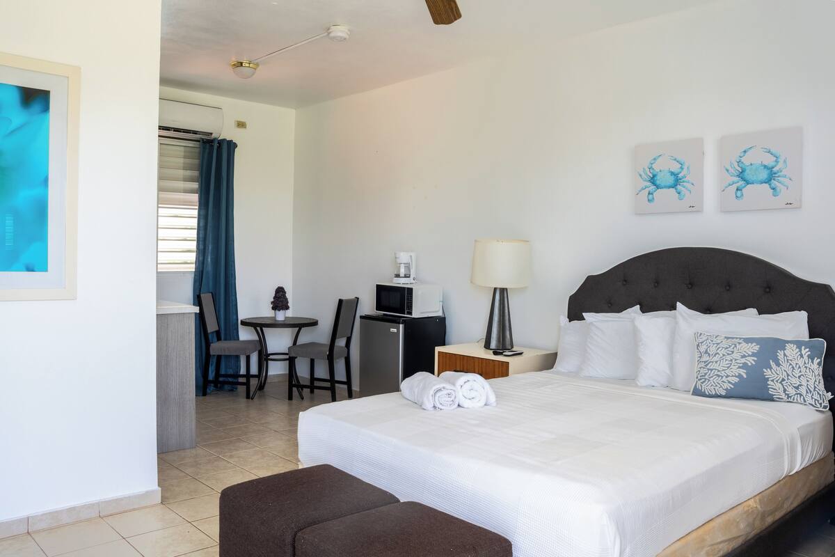 Habitación de hotel con cama, escritorio, silla, microondas, lámpara y obras de arte en la pared.