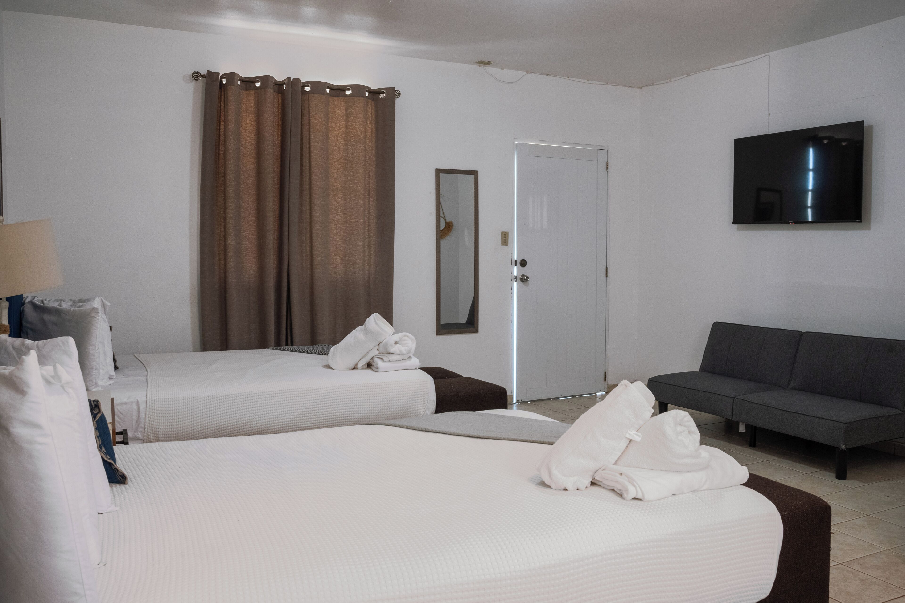 A hotel room with two beds, a sofa, a TV, and a door.