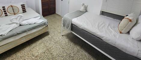 A bedroom with two beds, a wardrobe, an air conditioning unit, and a window with blinds.