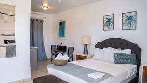 Ein Hotelzimmer mit einem großen Bett, einem Schreibtisch, einem Stuhl, einer Lampe und Kunstwerken an den Wänden.