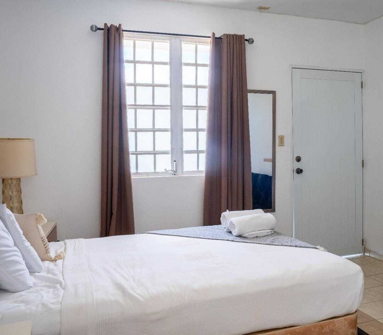 A hotel room with a bed, a window with curtains, a bedside lamp, and a door.