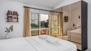 Une chambre avec un grand lit, une armoire, une bibliothèque et un balcon avec vue.
