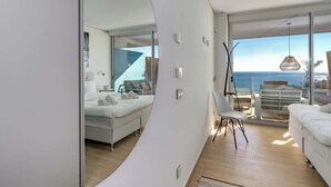 Une chambre moderne avec un grand lit, un fauteuil et une vue sur la mer grâce à de grandes fenêtres.