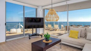 Un salon moderne avec un grand téléviseur, un canapé, une table basse et un luminaire suspendu en osier.