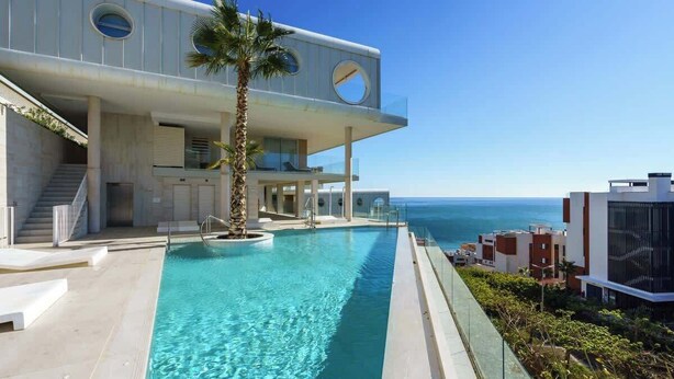 Un bâtiment moderne doté d’une piscine, de palmiers et offrant une vue sur l’océan.